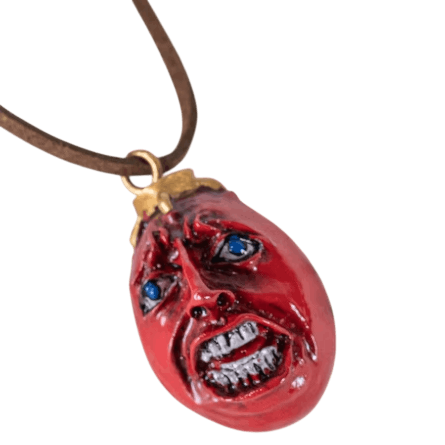 Pendentif Behelit porté au cou sur son cordon de cuir, gros plan sur le visage sculpté et la bélière dorée