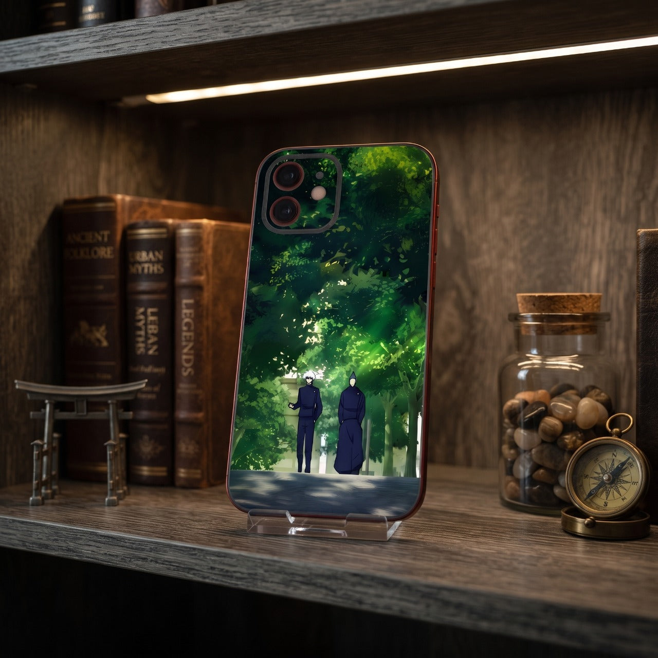 Coque iPhone Jujutsu Kaisen Gojo et Geto sur un support, étagère en bois avec livres anciens, torii miniature et boussole