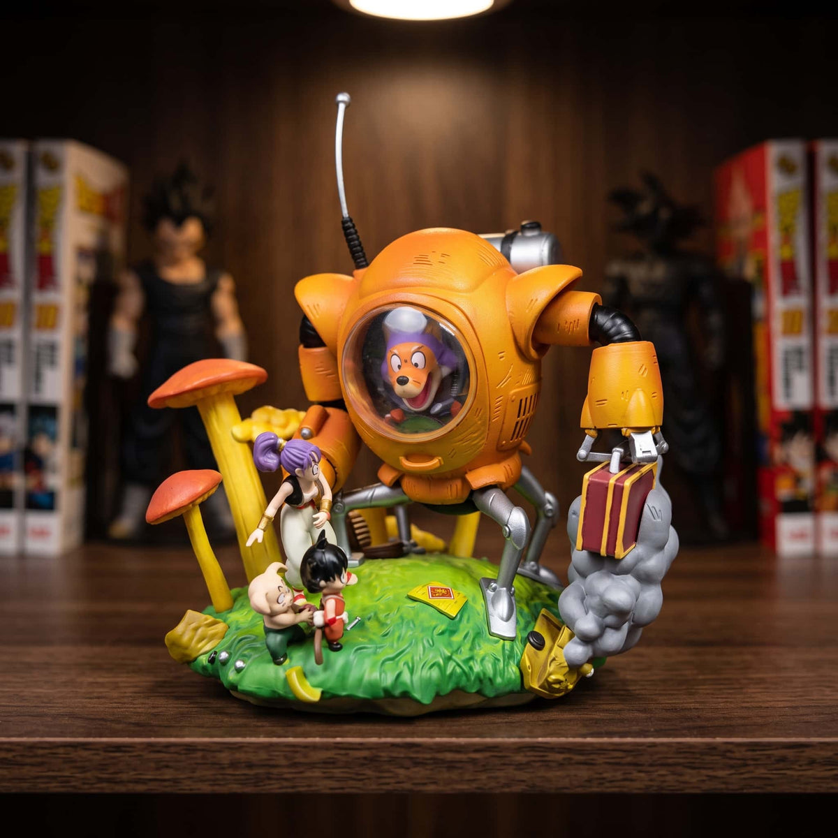 Diorama Dragon Ball : le robot orange de Shu à cockpit vitré face à Son Goku enfant, Bulma et Oolong, sur une prairie de champignons géants, 10 cm posé sur une étagère en bois