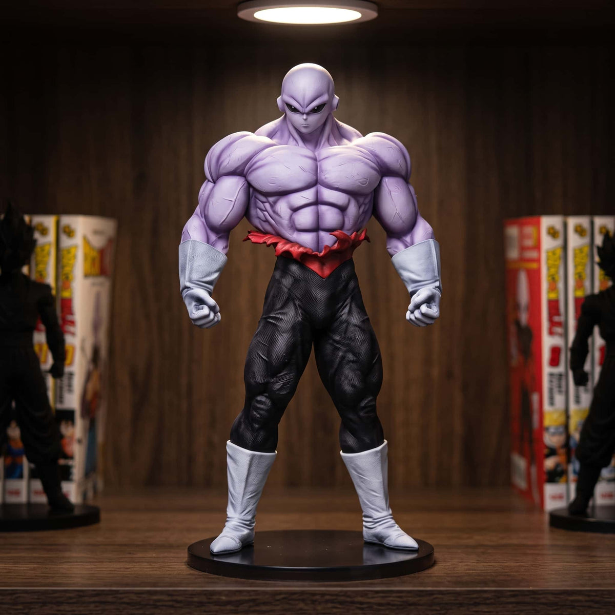 Figurine de Jiren de Dragon Ball Super : peau violette, combinaison noire et ceinture rouge, debout bras le long du corps, 26 cm sur socle noir, posée sur une étagère en bois