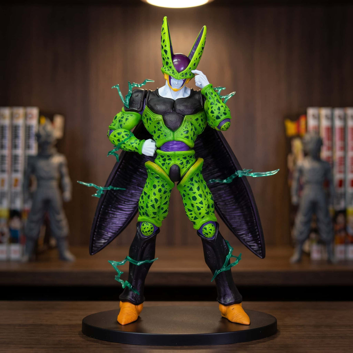 Figurine de Cell forme parfaite : carapace verte tachetée de noir, crête orange, collerette blanche, ailes repliées et éclats d'énergie verts translucides, 35 cm sur socle noir, posée sur une étagère en bois