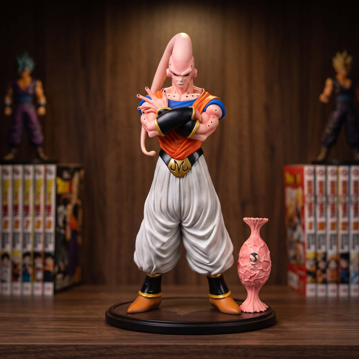Figurine de Majin Buu après l'absorption de Gohan, 27 cm, bras croisés, gilet orange et pantalon blanc, posée sur une étagère en bois avec son cocon rose à côté