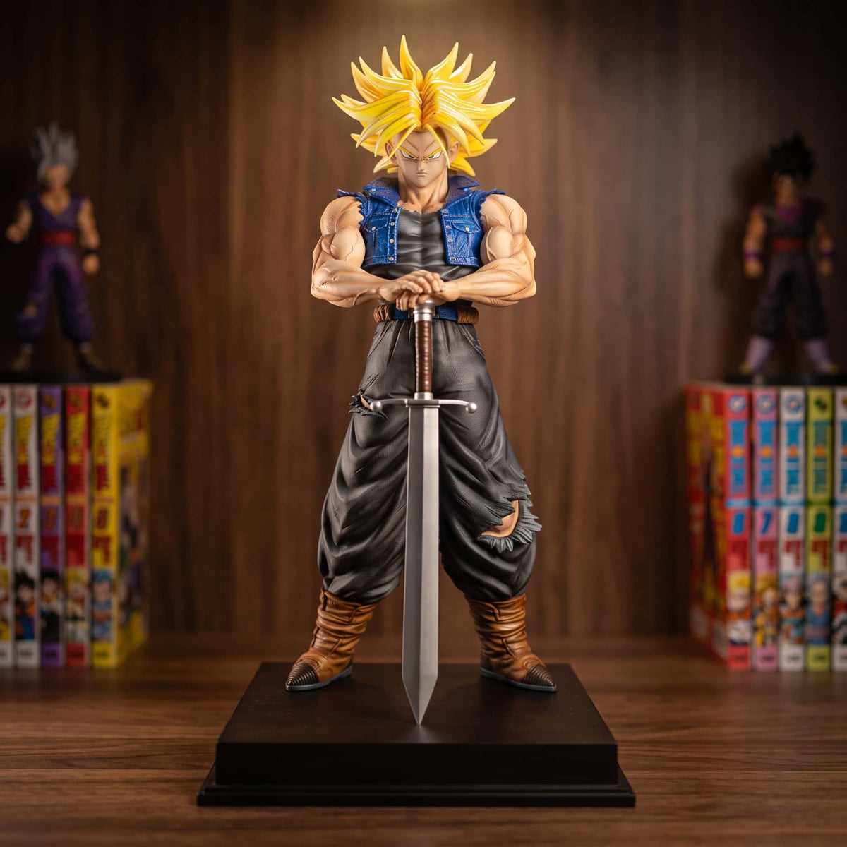 Figurine de Trunks du Futur en Super Saiyan, 53 cm, mains posées sur le pommeau de son épée plantée, gilet en jean bleu, sur une étagère en bois avec des tomes de manga