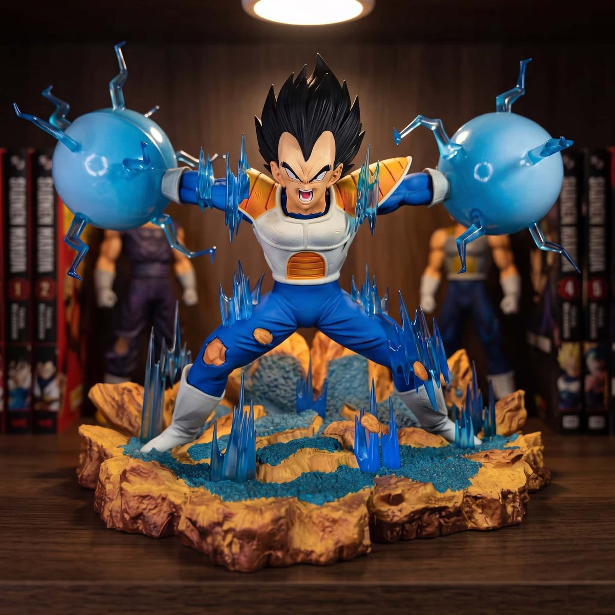 Figurine de Vegeta en armure saiyan tenant une sphère d'énergie bleue dans chaque main, socle de roche ocre hérissé de cristaux bleus, 22 cm de haut sur 30 de large, posée sur une étagère en bois