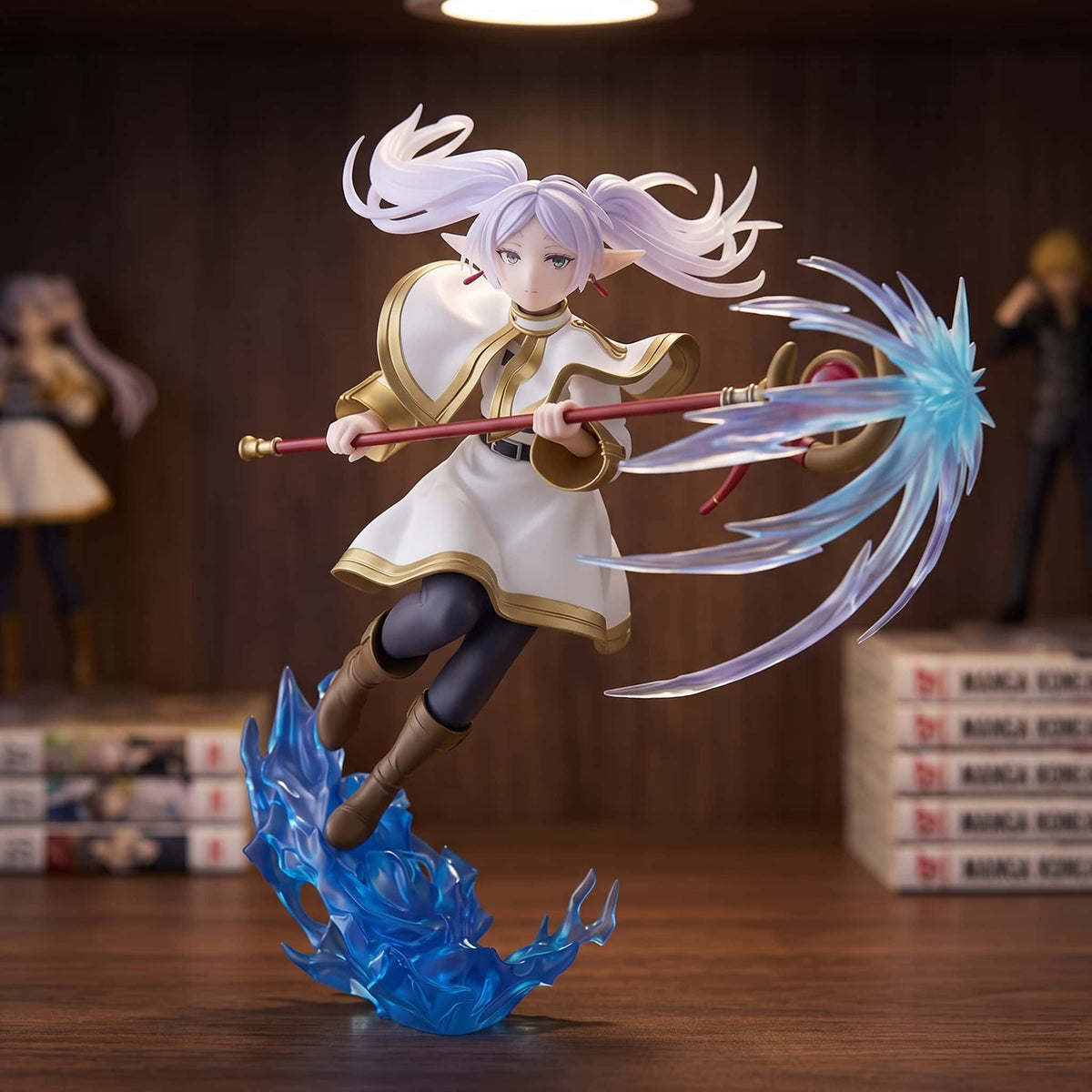 Figurine Frieren 21 cm en plein élan, bâton tendu et sort bleu, exposée sur une étagère devant des mangas (décor non inclus)
