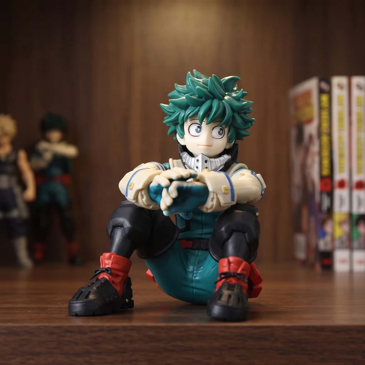 Figurine d'Izuku Midoriya assis au sol, avant-bras croisés sur les genoux, costume vert et col-masque blanc, 10 cm, posée sur une étagère en bois