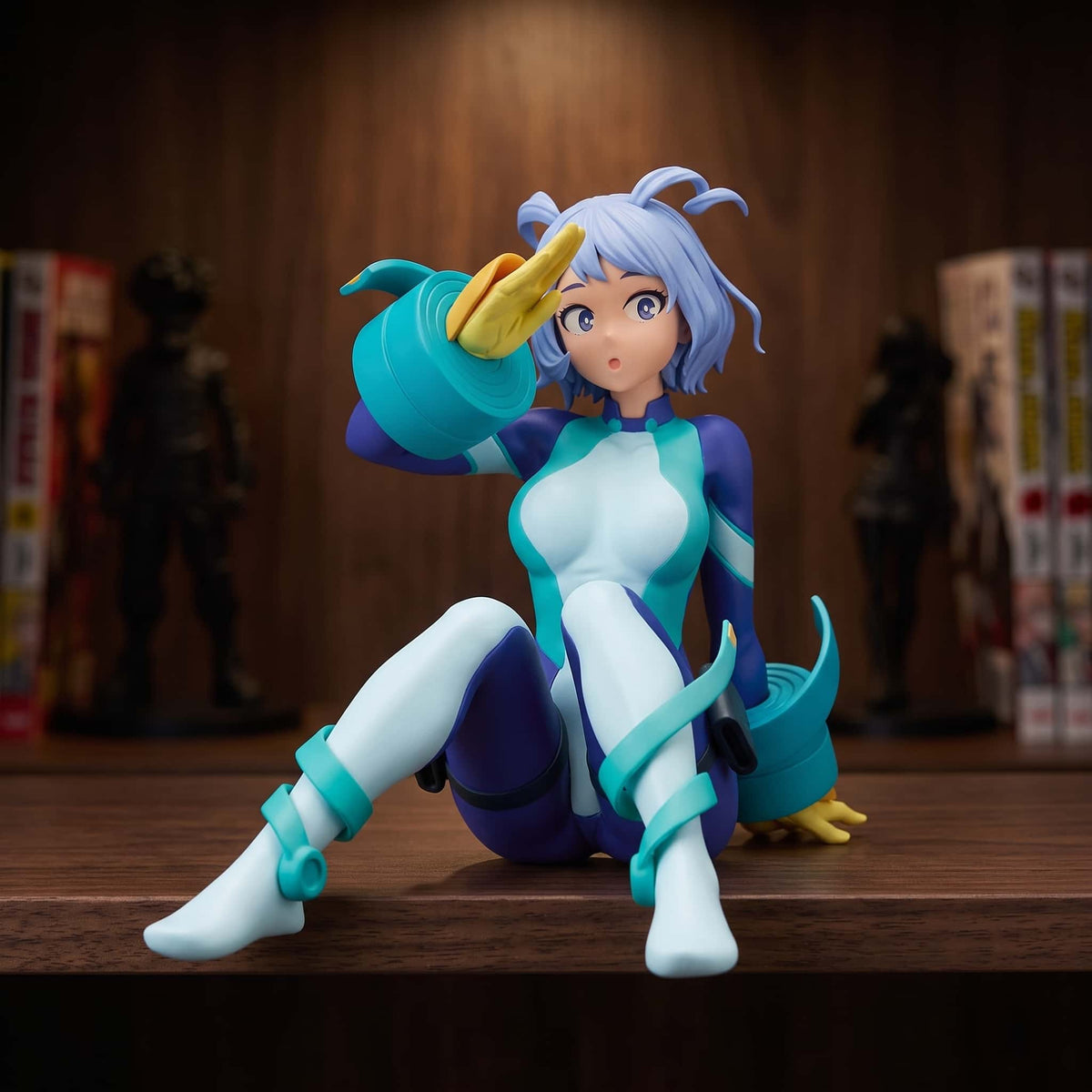 Figurine de Nejire Hado assise au sol, main portée au front en salut, combinaison bleu nuit et turquoise, cheveux bleu clair, 11 cm, posée sur une étagère en bois