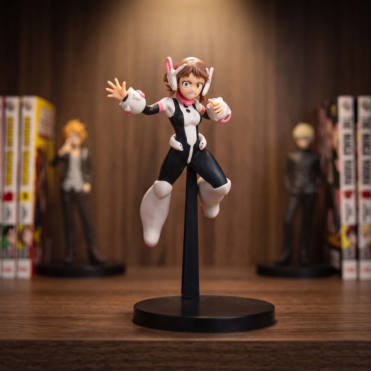 Figurine d'Ochaco Uraraka en suspension au-dessus de son socle, combinaison noire à empiècements roses et casque à antennes, 18 cm, posée sur une étagère en bois