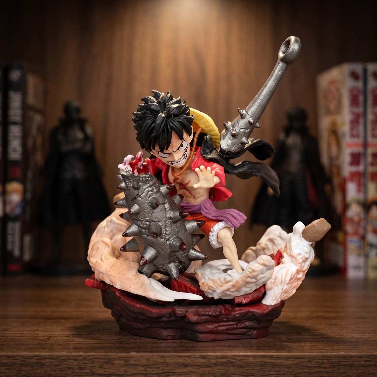 Figurine chibi One Piece Luffy 10 cm face à une massue à pointes géante, exposée sur une étagère devant des mangas (décor non inclus)