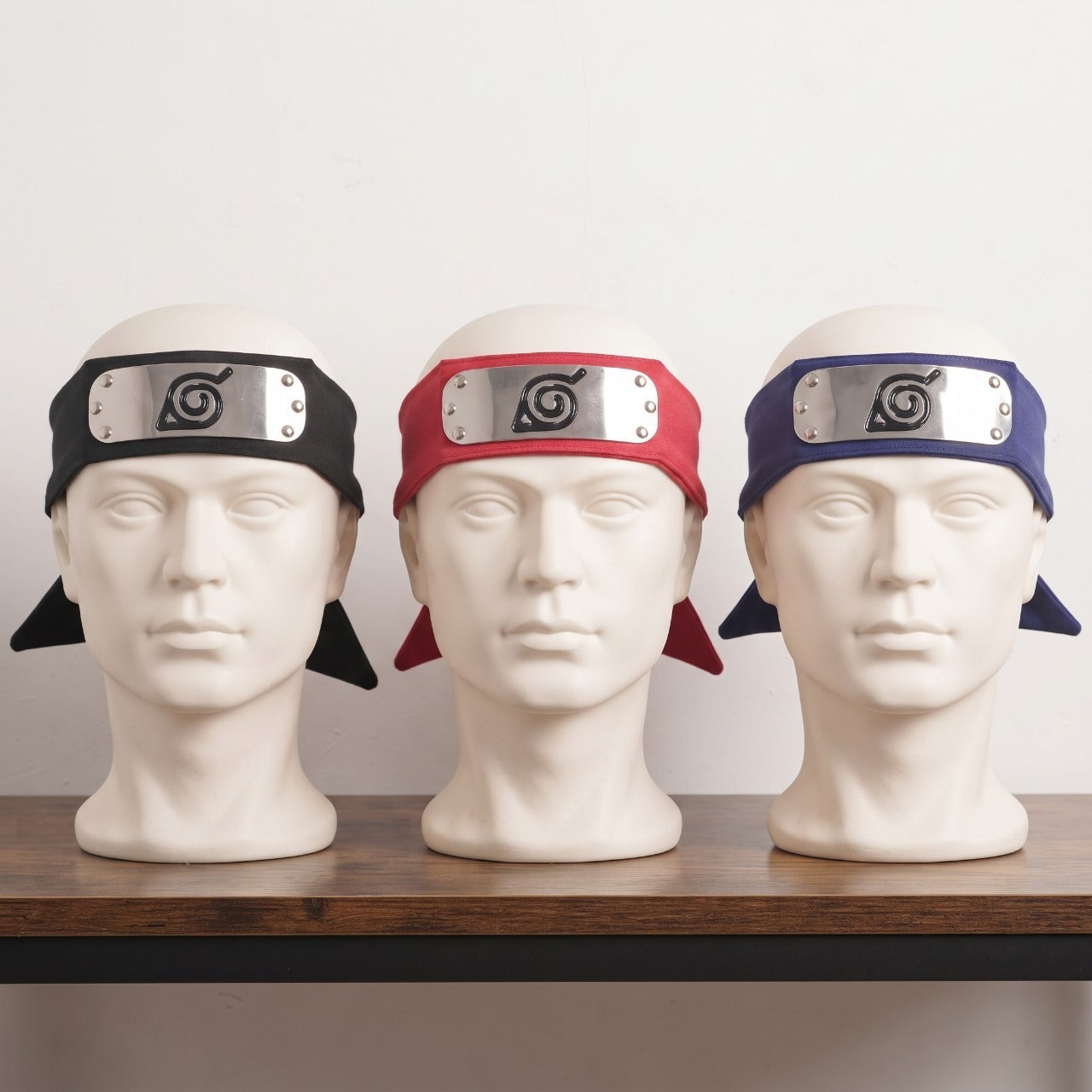 Trois bandeaux ninja de Konoha, noir, bleu marine et rouge, posés en éventail sur une table en bois