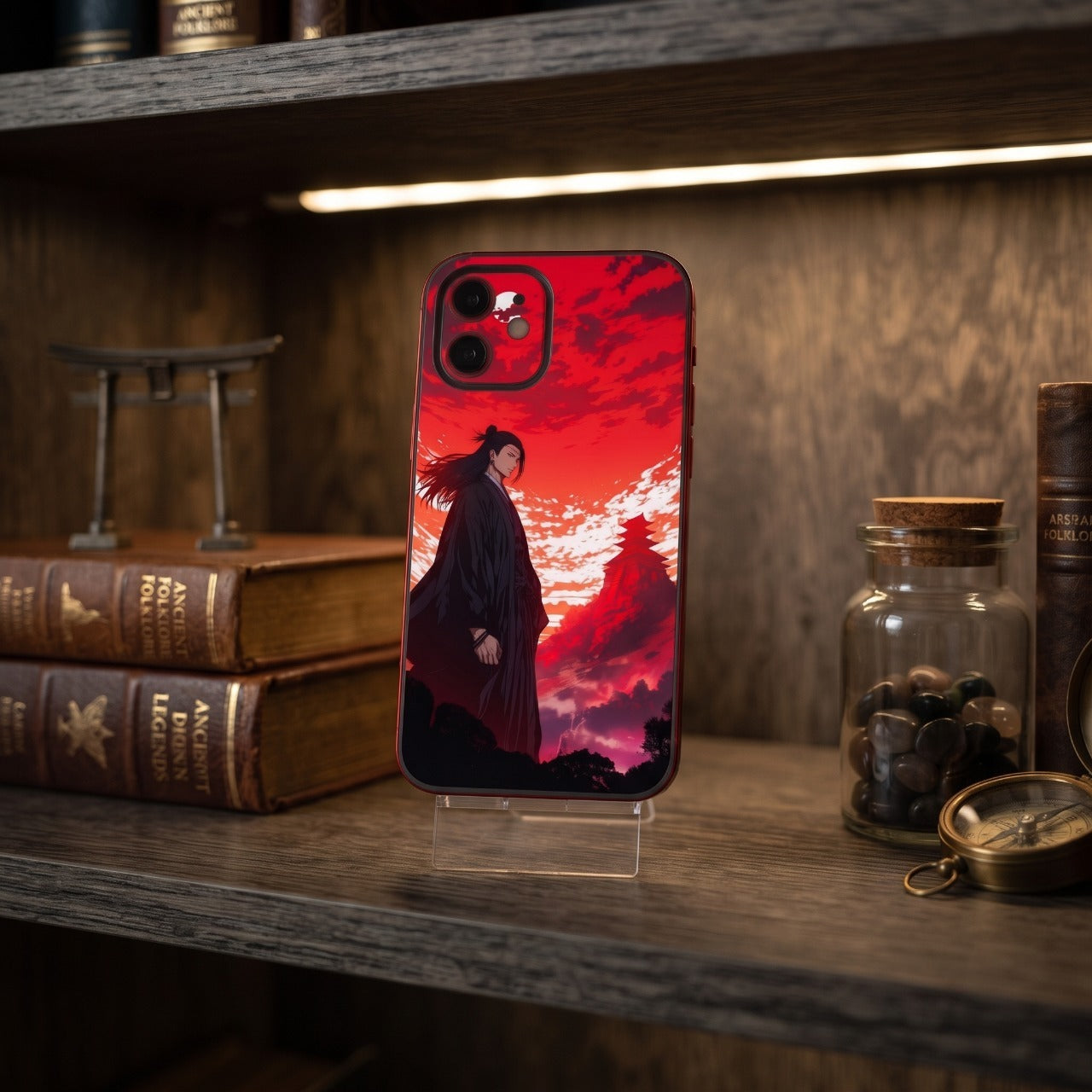 Coque iPhone Jujutsu Kaisen Geto sur un support, étagère en bois avec livres anciens, torii miniature et boussole