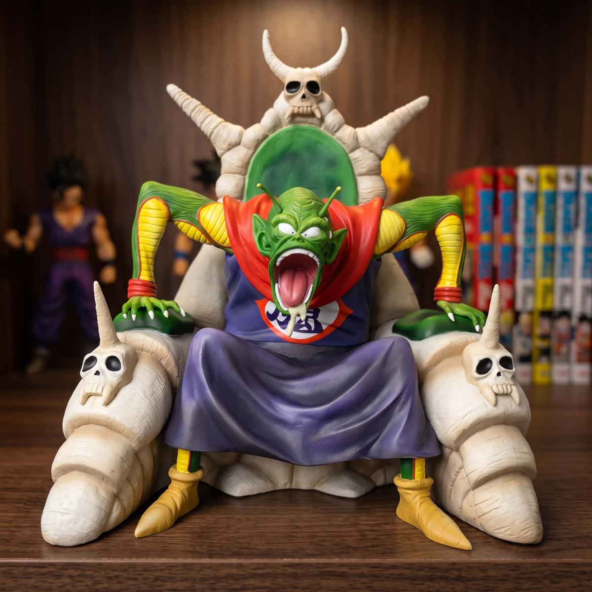 Figurine Dragon Ball Piccolo Daimaô 28 cm sur son trône d'os, exposée sur une étagère devant des mangas (décor non inclus)