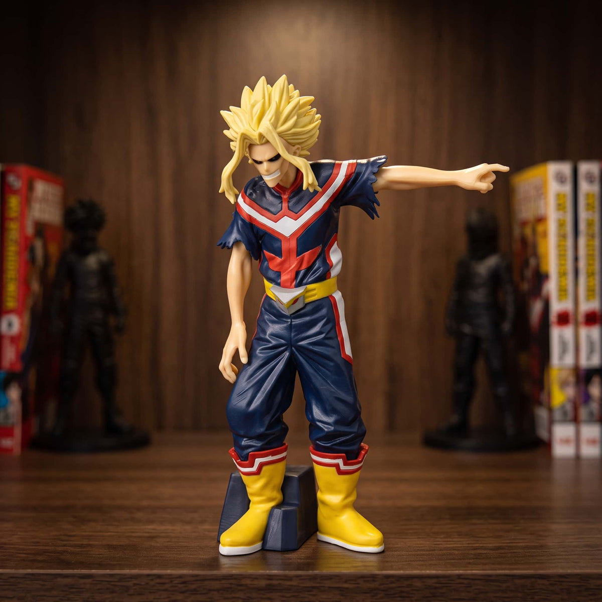 Figurine d'All Might bras droit tendu et index pointé, costume bleu marine à plastron rouge et blanc, 18 cm, posée sur une étagère en bois
