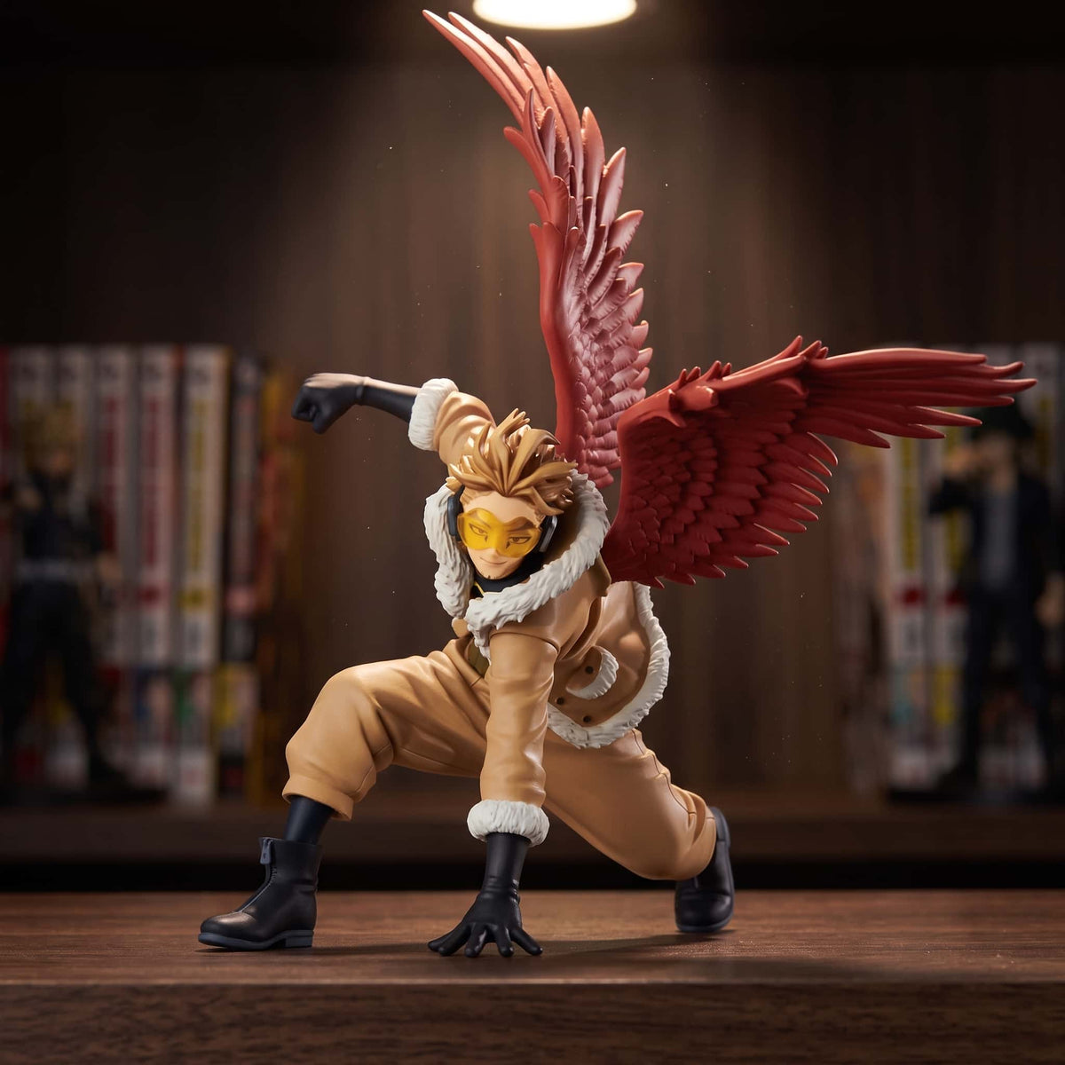 Figurine de Hawks un genou à terre, grandes ailes rouges déployées, manteau beige à col fourré et lunettes jaunes, 11 cm, posée sur une étagère en bois