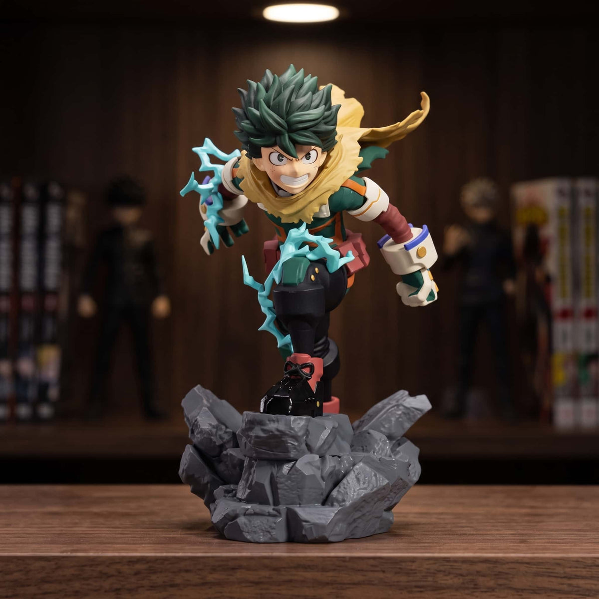Figurine d'Izuku Midoriya en plein élan, éclairs verts translucides le long des bras et des jambes, écharpe jaune au vent, 12 cm sur socle rocheux, posée sur une étagère en bois