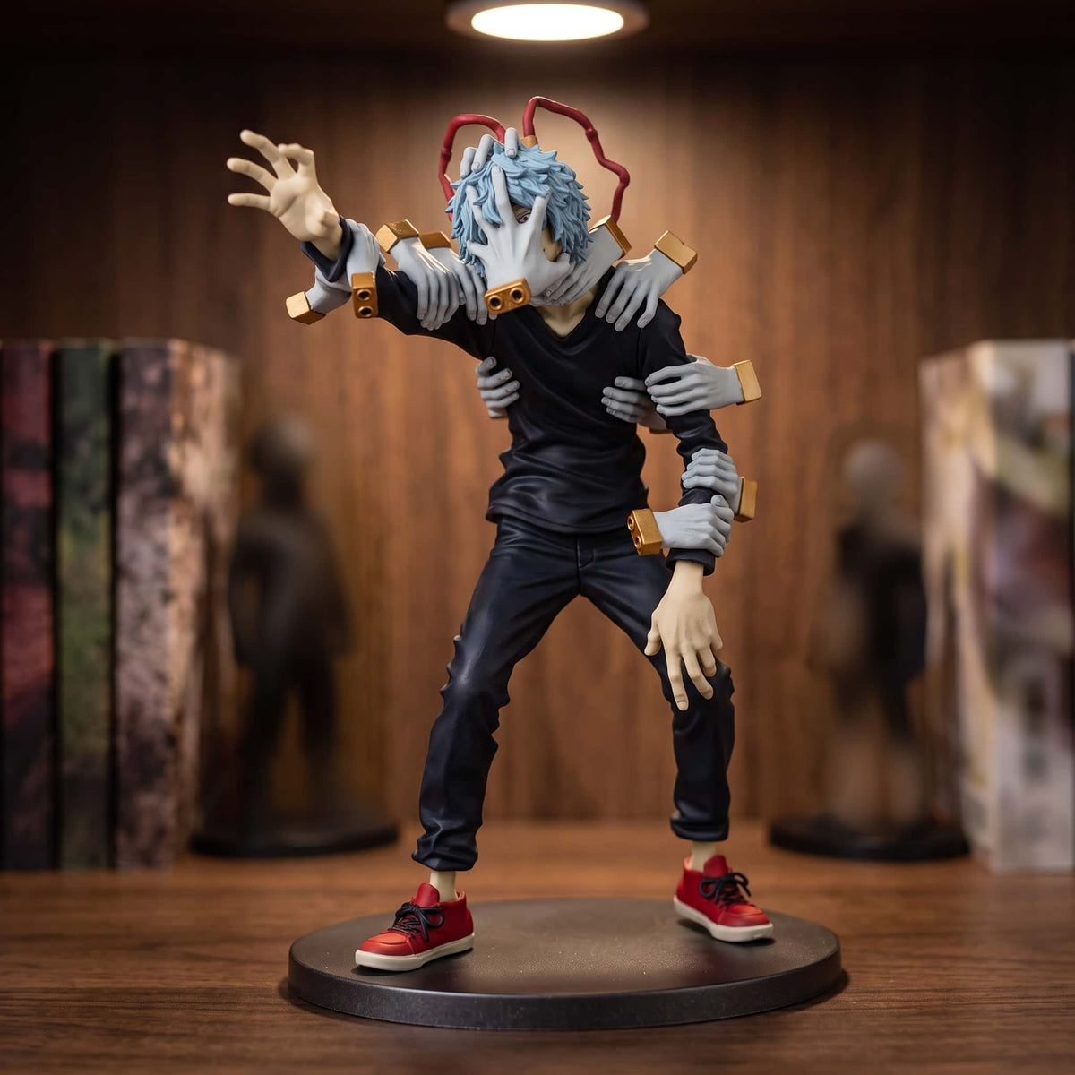 Figurine de Tomura Shigaraki, mains accrochées aux épaules et au visage, main tendue vers l'avant, haut noir et baskets rouges, sur un socle noir posé sur une étagère en bois