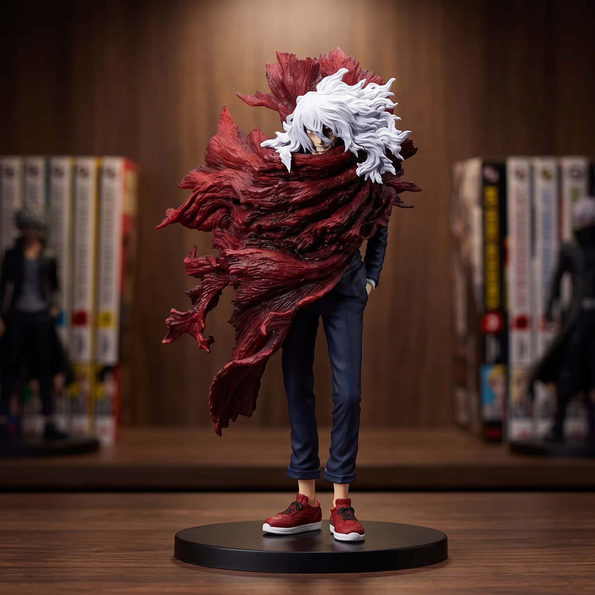Figurine de Shigaraki Tomura, mains dans les poches, avec une immense vague de décomposition rouge sculptée en volutes derrière lui, sur un socle noir posé sur une étagère en bois