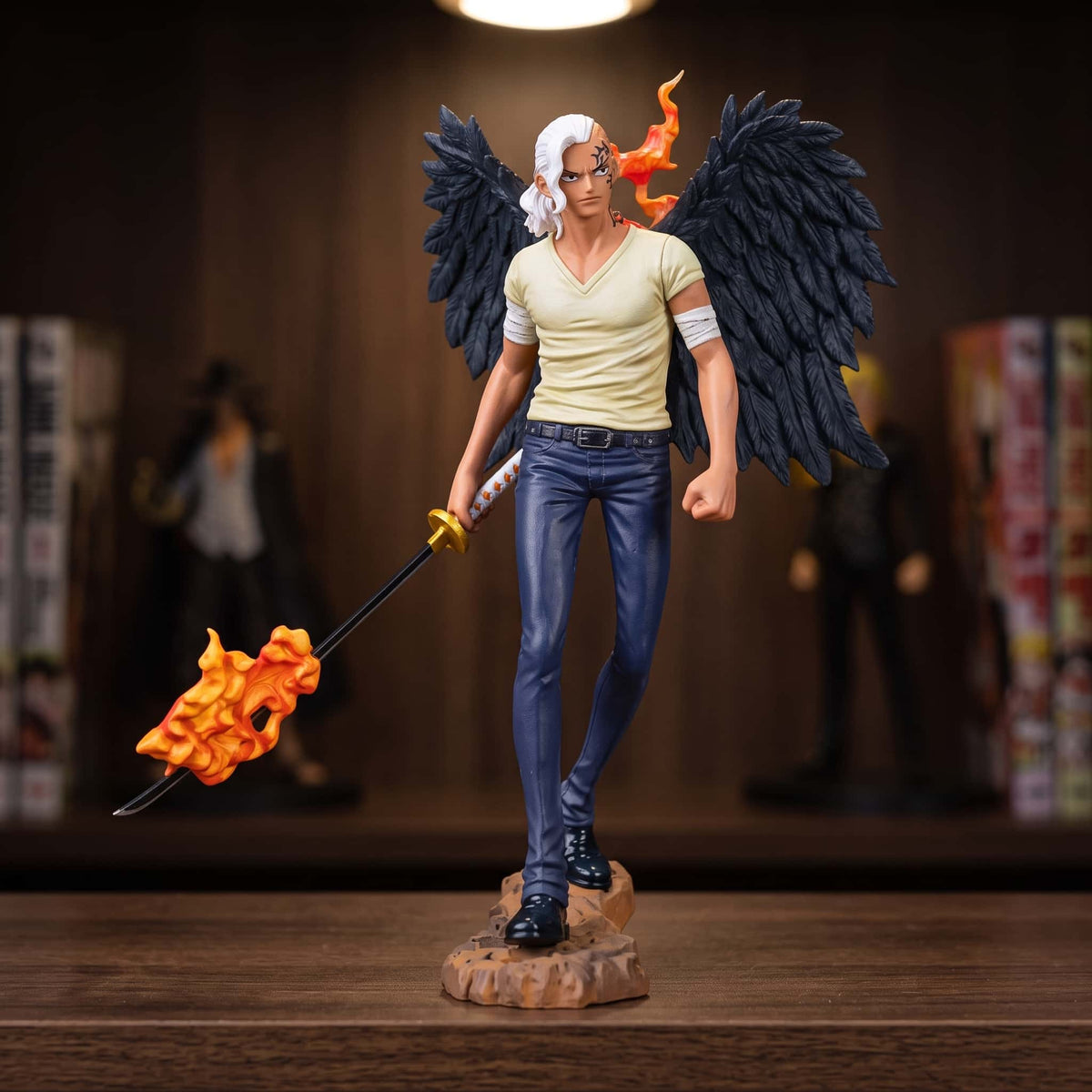 Figurine One Piece King jeune 15 cm, ailes noires déployées et sabre en flammes, exposée sur une étagère devant des mangas (décor non inclus)