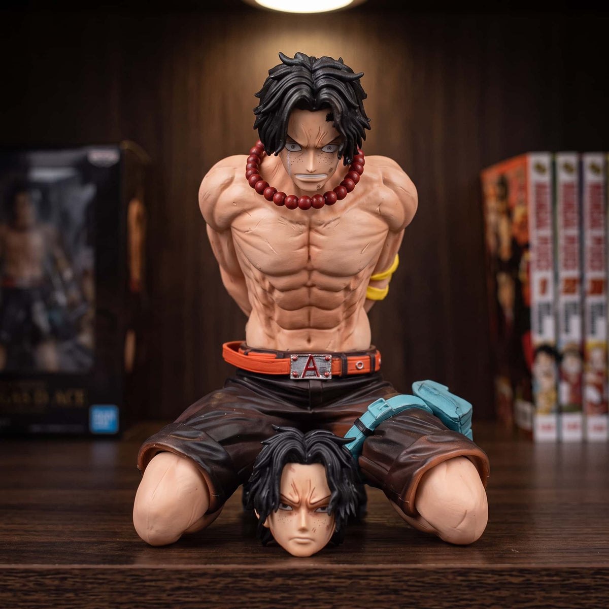 Figurine One Piece Portgas D. Ace 13 cm à genoux et enchaîné, exposée sur une étagère devant des mangas (décor non inclus)