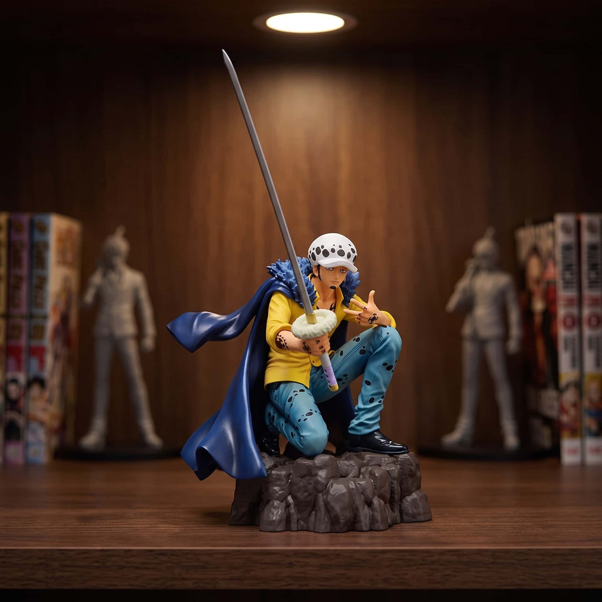 Figurine One Piece Trafalgar Law 13 cm un genou à terre, Kikoku dressé, exposée sur une étagère devant des mangas (décor non inclus)