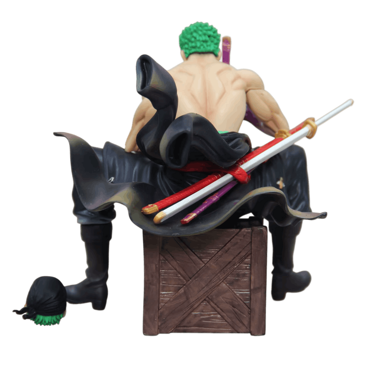 Figurine Zoro One Piece de dos : dos nu, manteau sombre étalé sur la caisse, fourreaux rouge et violet et sabre blanc noués, seconde tête au bandana noir