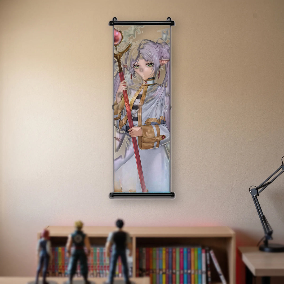 Kakémono Frieren, Frieren de face, le bâton posé sur l'épaule, tenue blanche à liseré doré, suspendu au mur beige d'une chambre au-dessus d'une étagère de tomes de manga