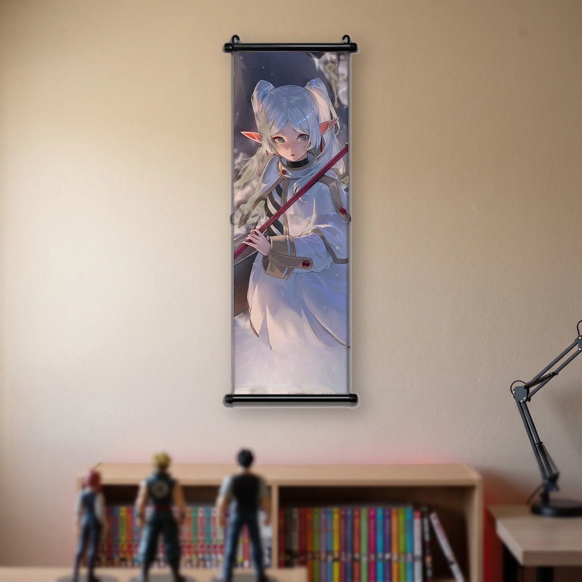 Kakémono Frieren, Frieren debout, bâton en diagonale, sur un fond sombre, suspendu au mur beige d'une chambre au-dessus d'une étagère de tomes de manga