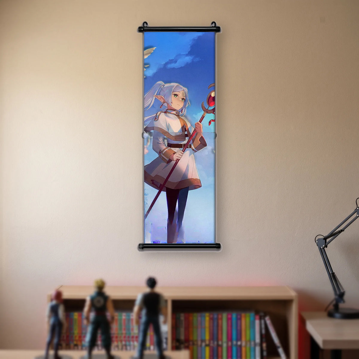 Kakémono Frieren, Frieren debout, bâton planté, sous un grand ciel bleu, suspendu au mur beige d'une chambre au-dessus d'une étagère de tomes de manga