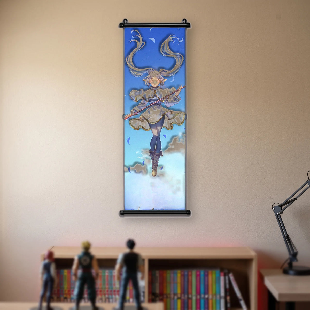 Kakémono Frieren, Frieren en lévitation, yeux clos, bâton horizontal, dans un ciel bleu, suspendu au mur beige d'une chambre au-dessus d'une étagère de tomes de manga