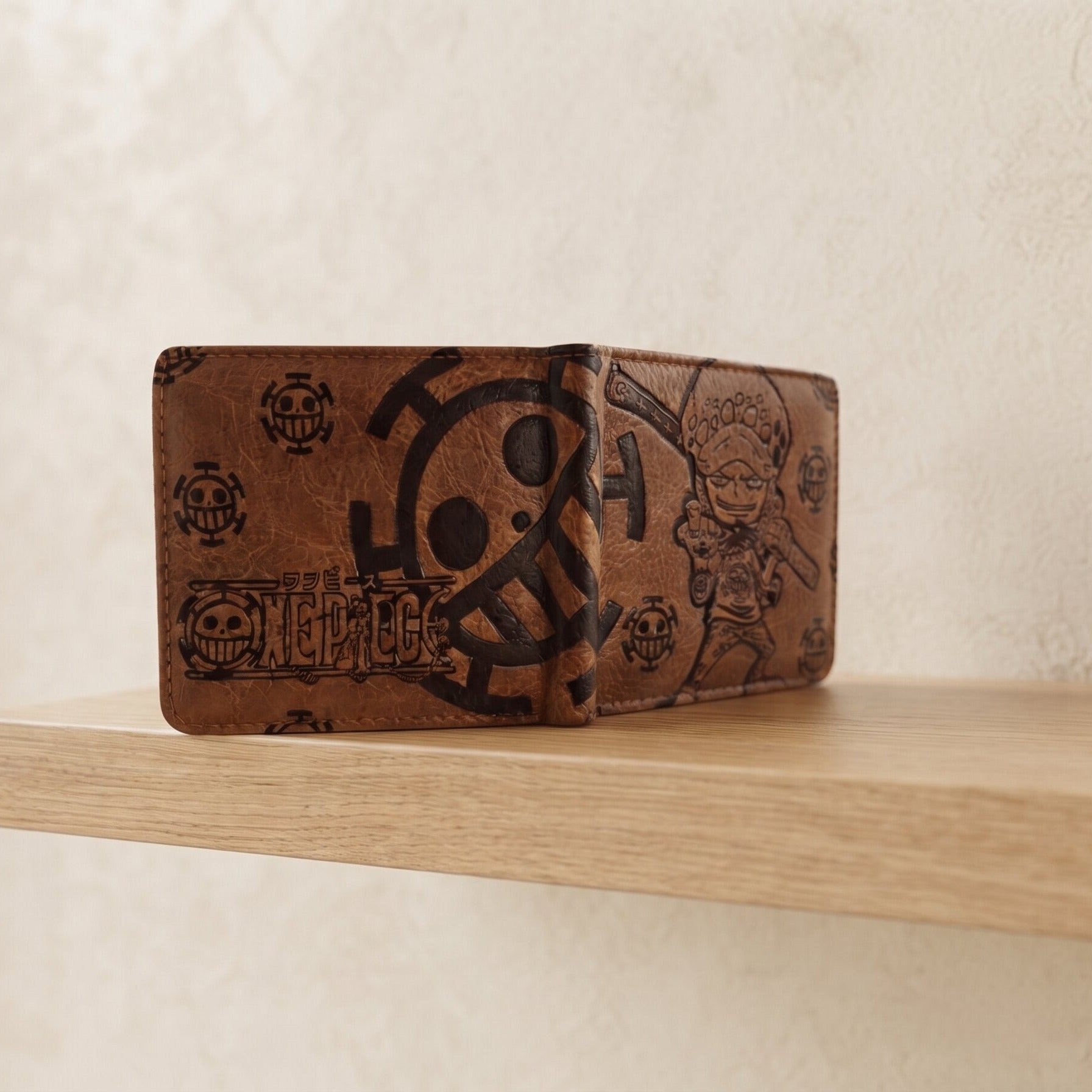 Portefeuille One Piece en similicuir brun gravé, posé fermé sur une étagère en bois clair